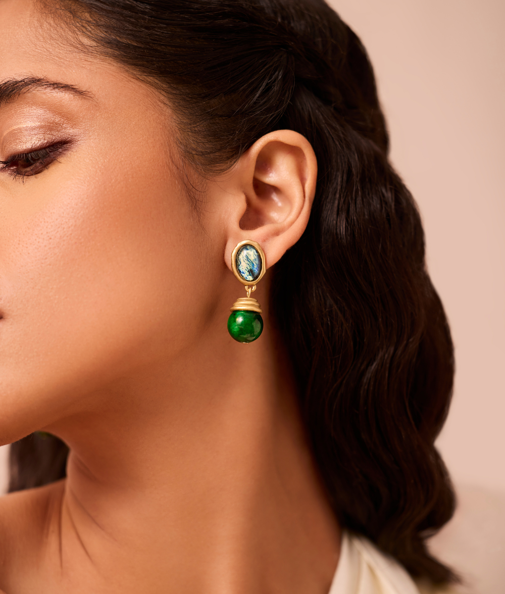 Close-up of a woman wearing green earrings with a neutral background