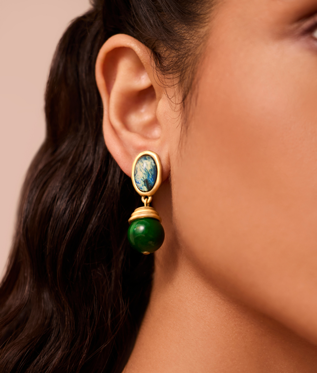 Close-up of a person wearing a gold earring with a green gemstone on a beige background