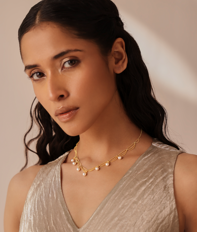 Woman wearing a gold necklace with pearls against a neutral background